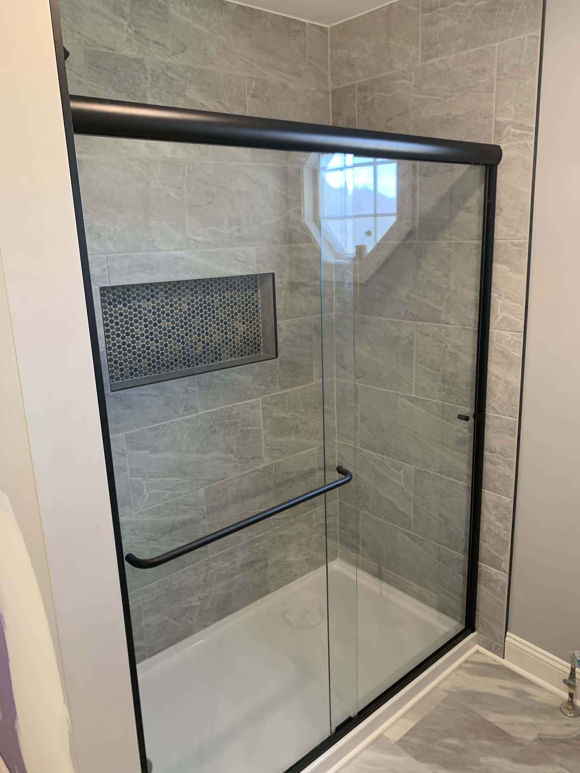 Walk-in shower with gray stone-look tile and sliding black frame glass in Lancaster, Ohio