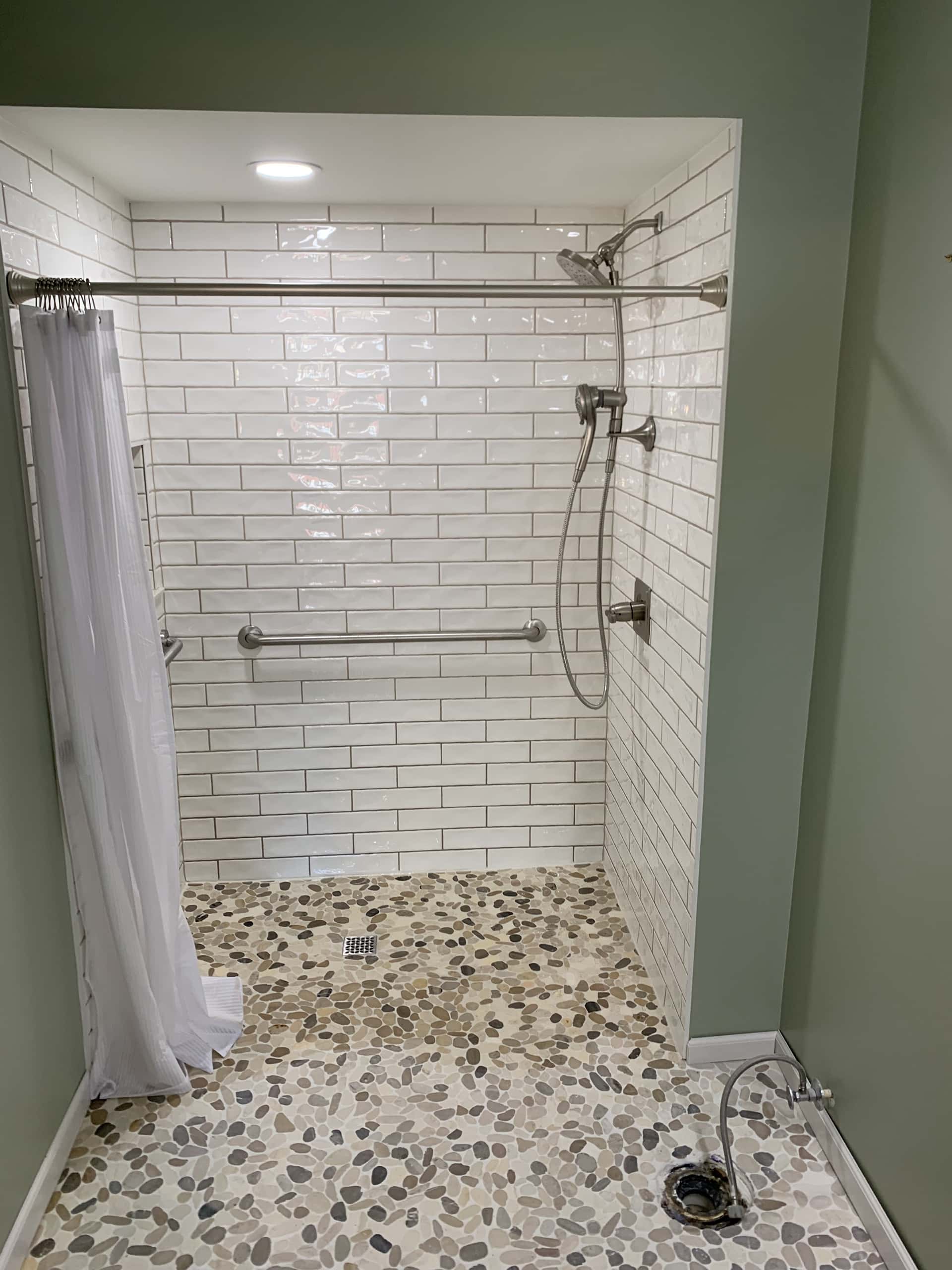 Accessible walk-in shower with white subway tile and pebble stone floor in Lancaster, Ohio